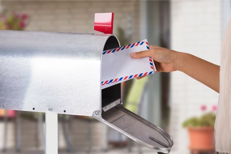 person putting an envelope to a metal mailbox